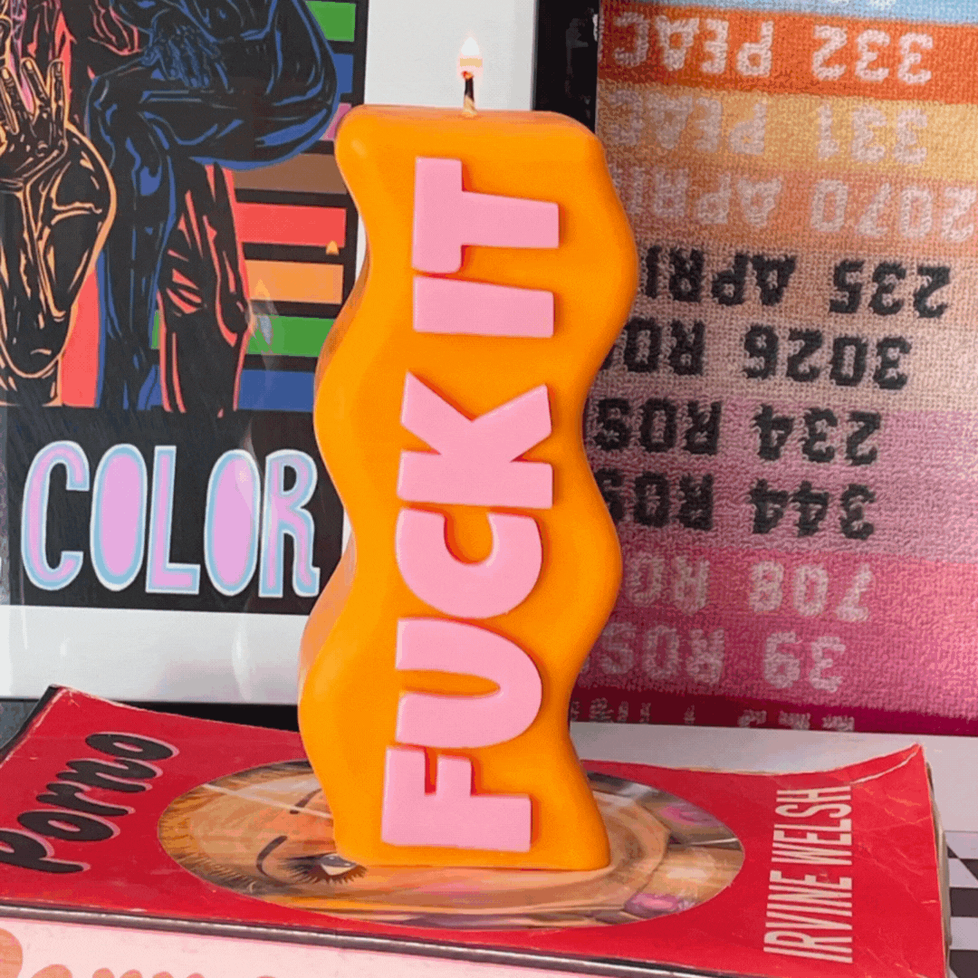 Orange sculptural candle with raised pink lettering and a lit wick